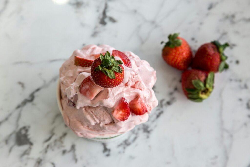 A bowl of homemade strawberry ice cream with fresh strawberries on a marble countertop.